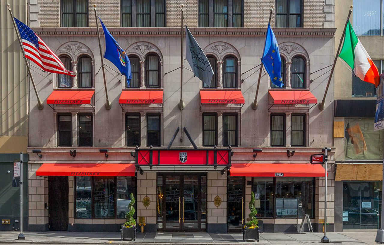 The Fitzpatrick Manhattan hotel façade with red awnings and flags above the entrance